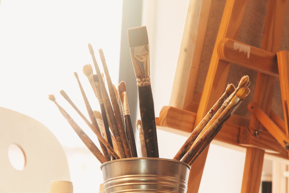 A collection of used paintbrushes in a metal container set in a warm, sunlit art studio.